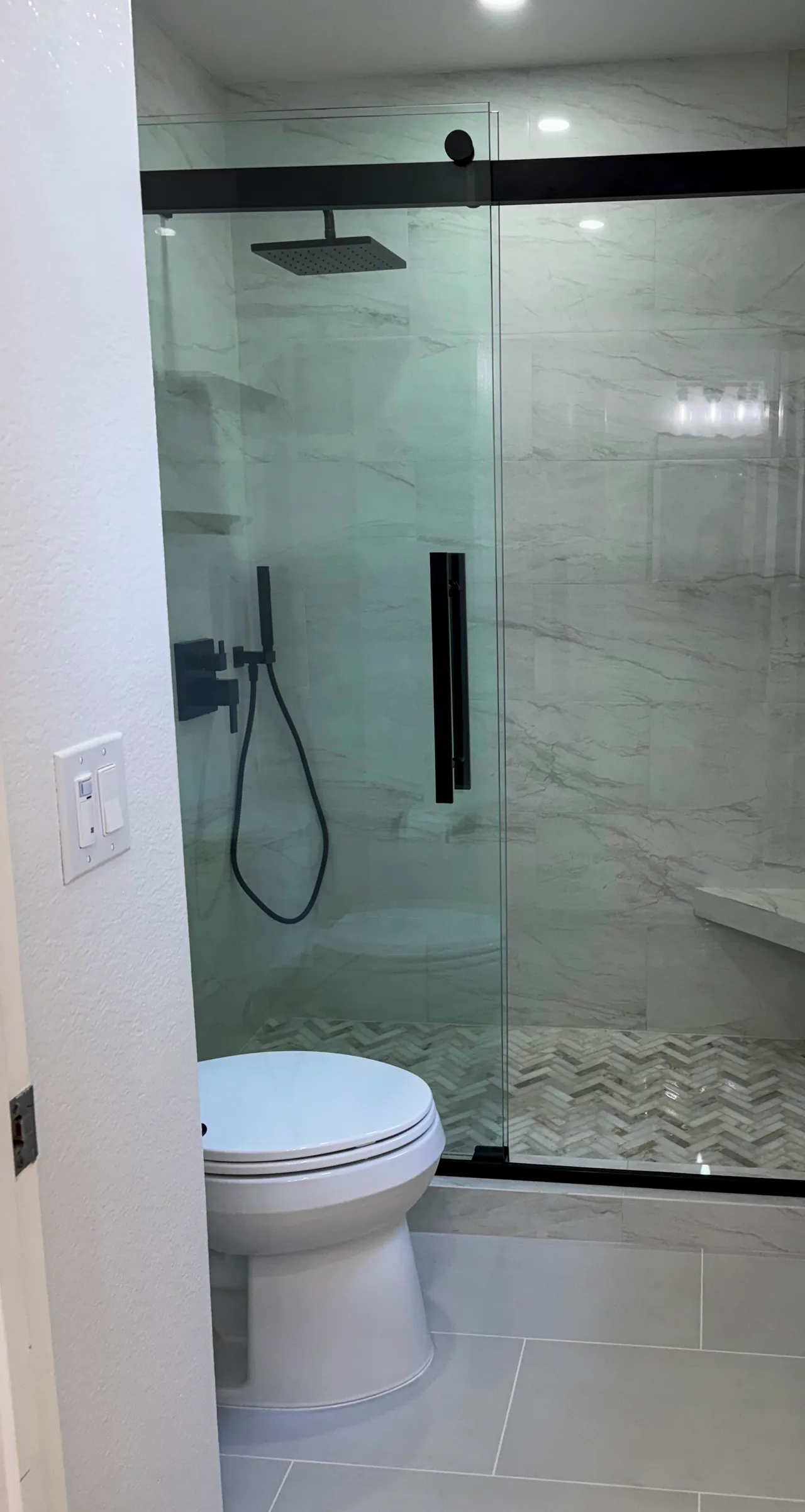Walk-in shower with marble-look tile walls, matte black fixtures and a herringbone floor