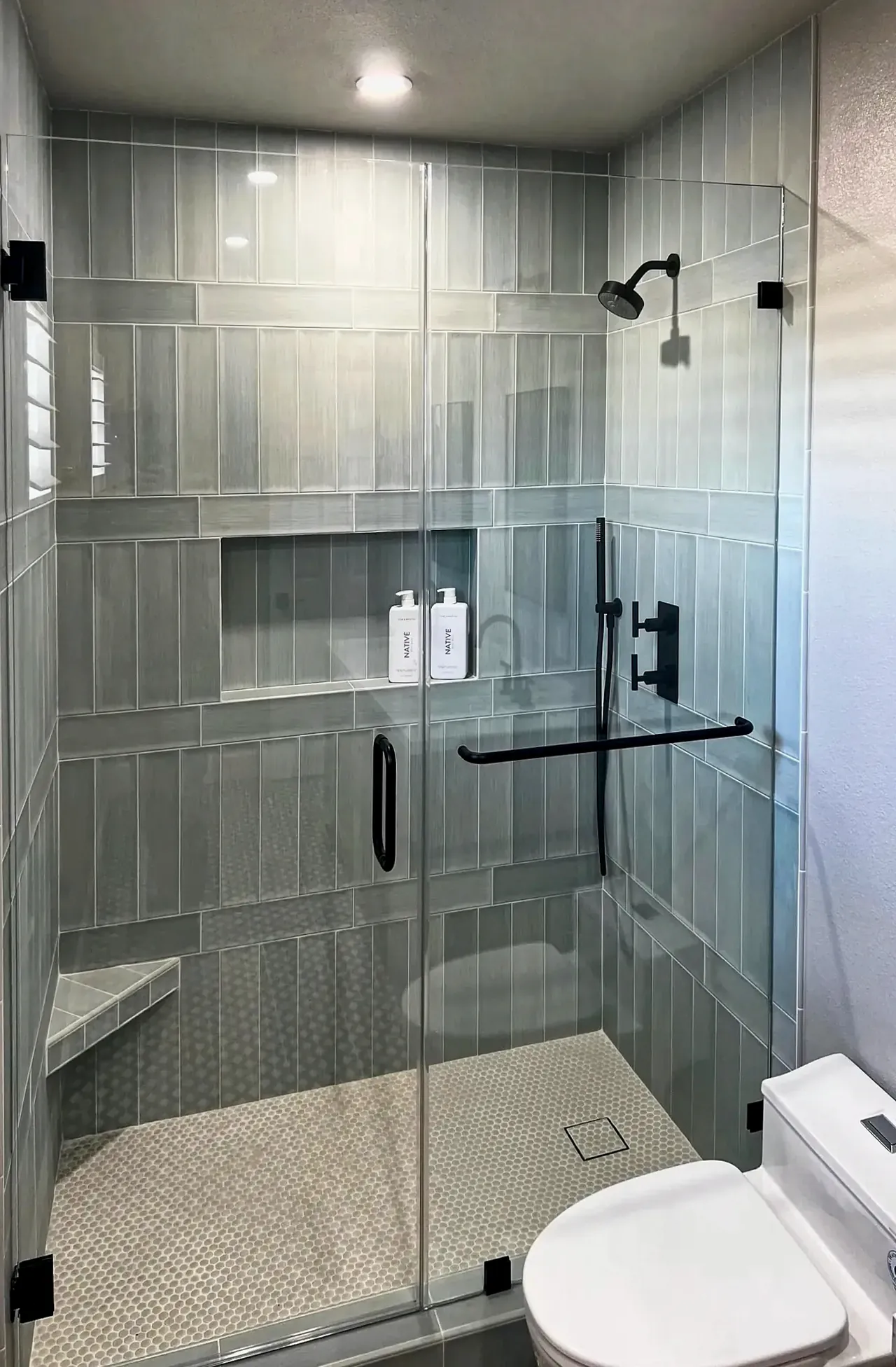 Shower tile with horizontal banding, a full-width niche, a corner bench and a penny-round pan