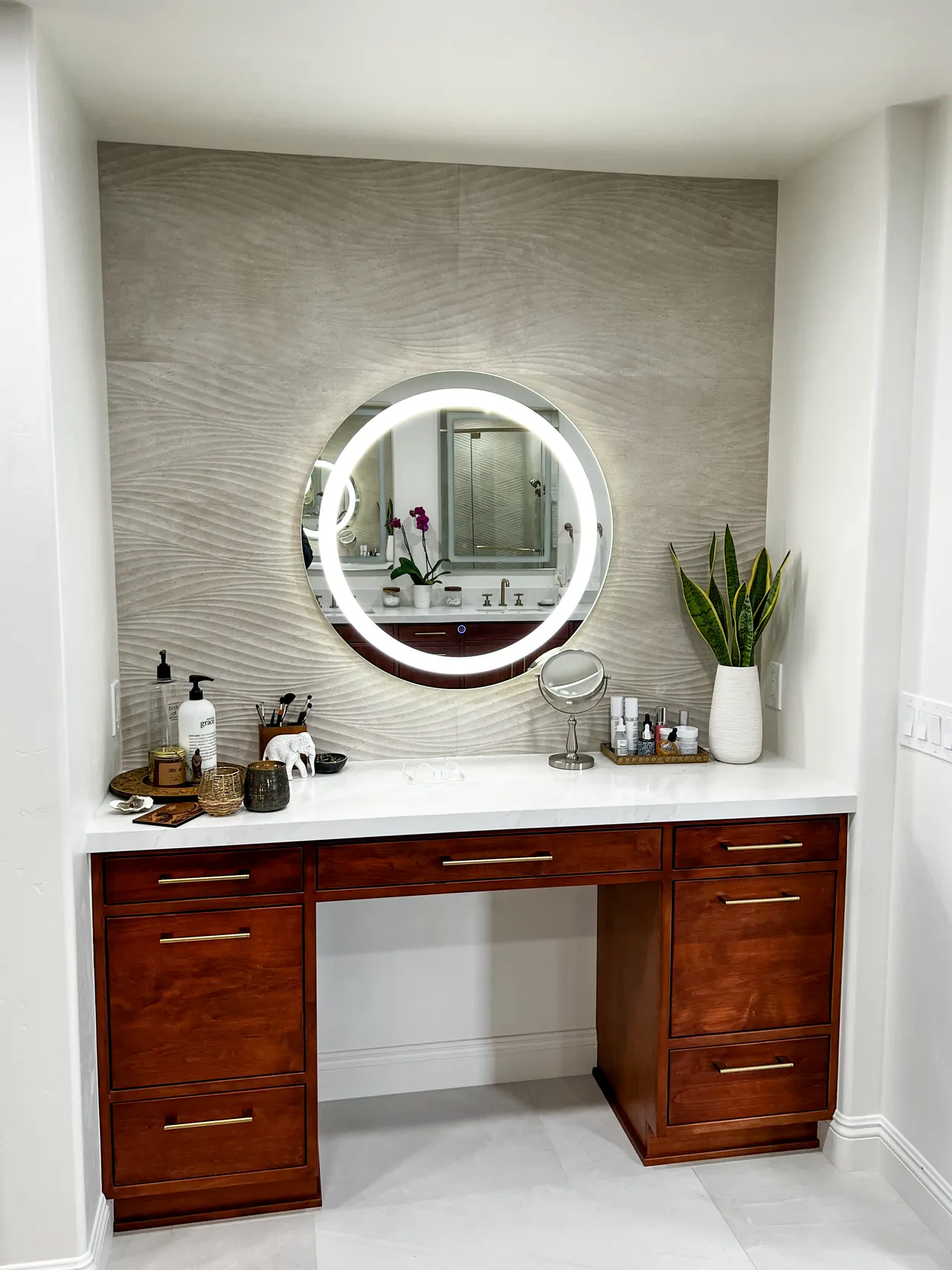 Separate makeup vanity with a lighted round mirror in front of a wave-pattern tile wall
