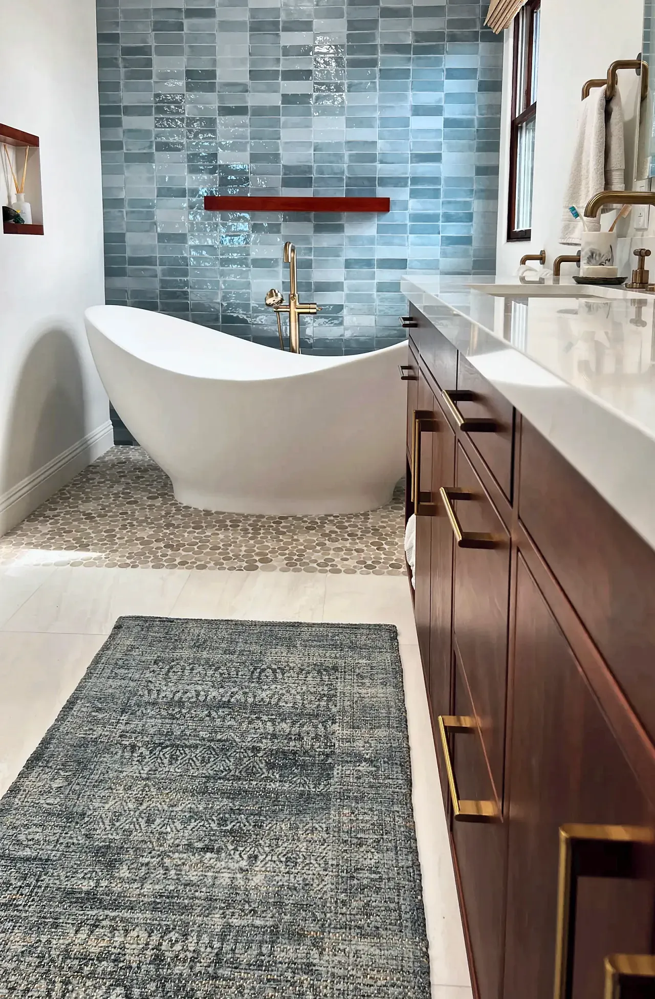 Freestanding tub in front of the blue tile feature wall, seen past the wood double vanity