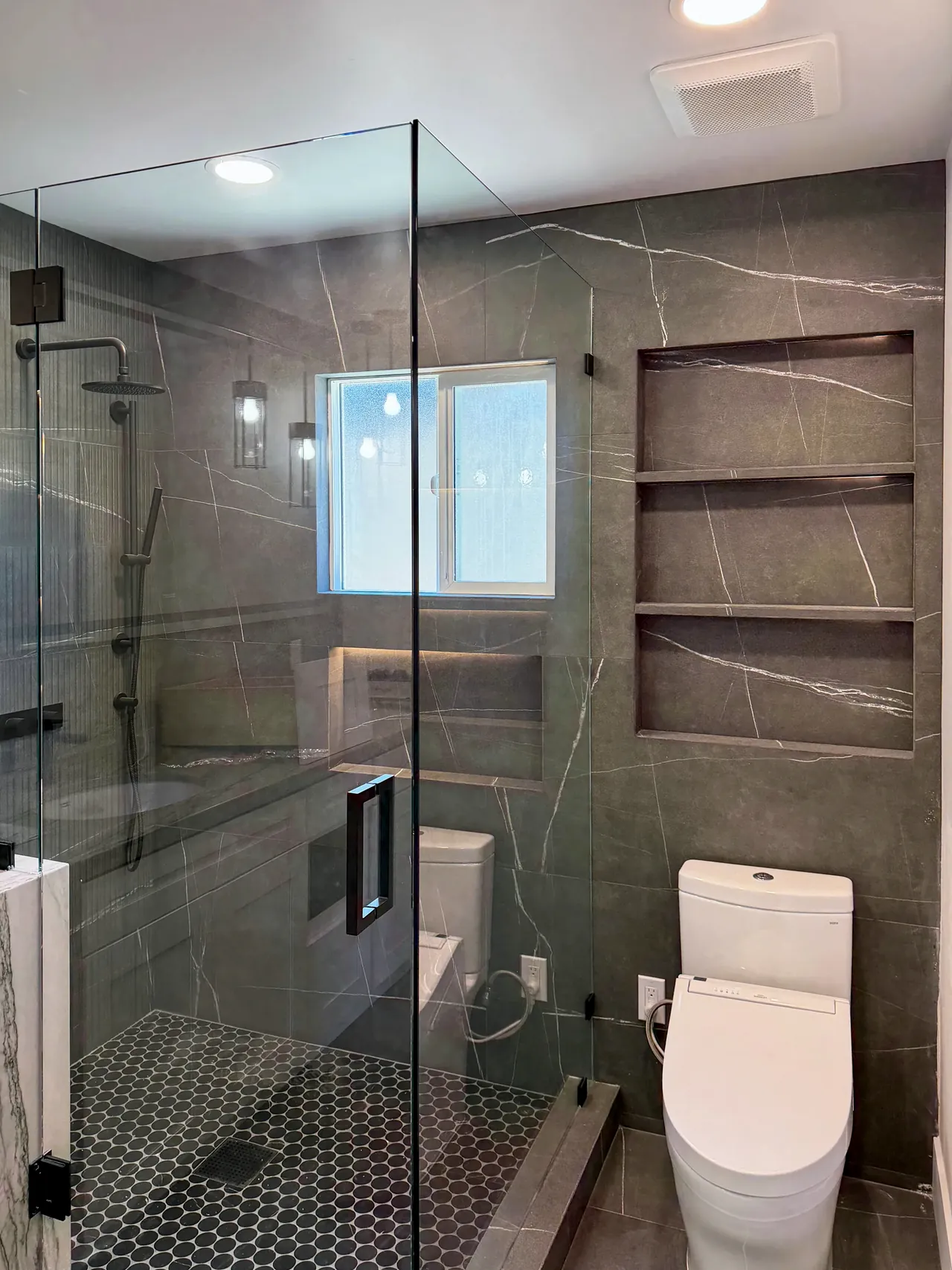 Primary bathroom with charcoal porcelain walls, frameless glass and lit niches