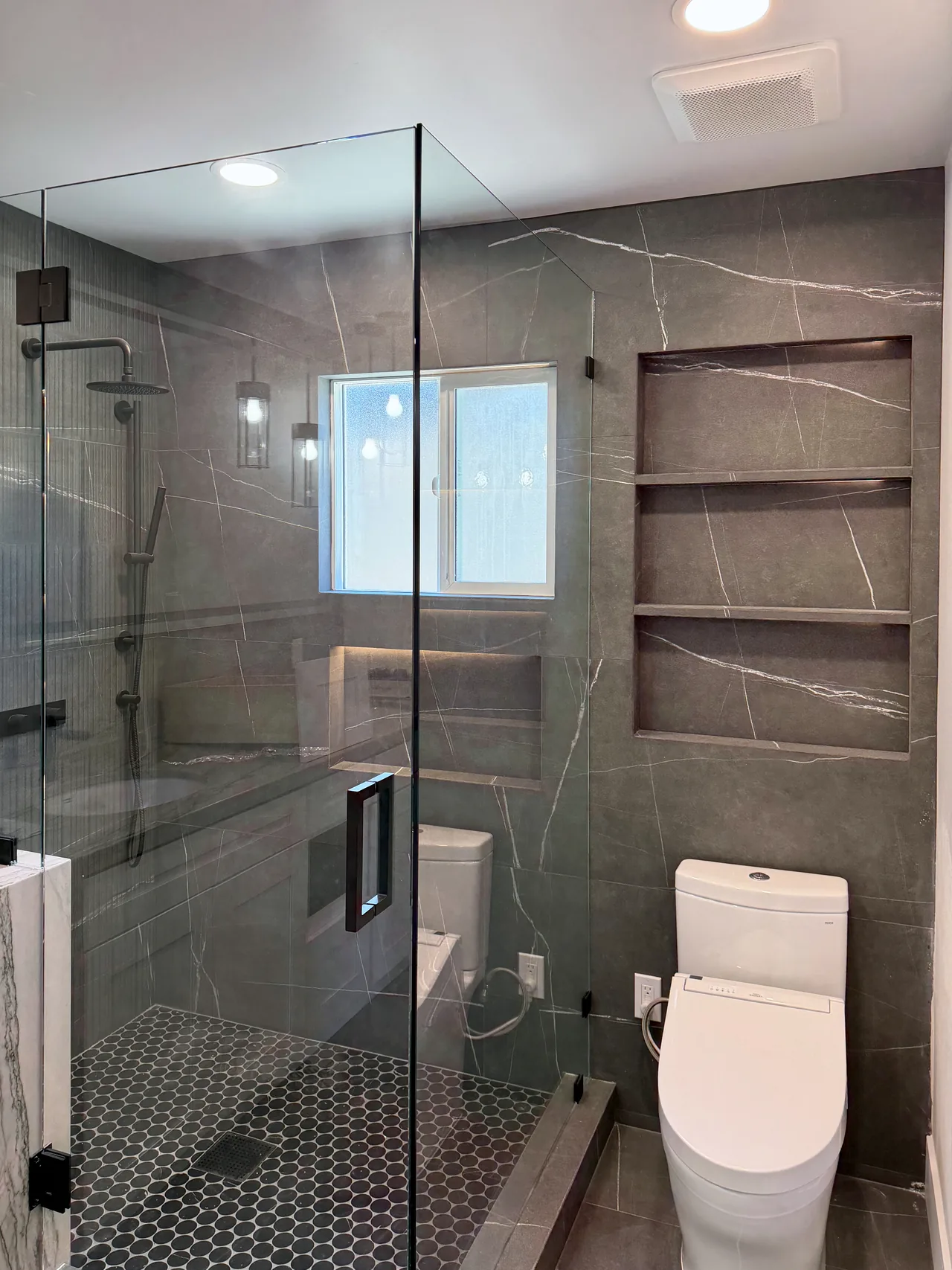 Primary bathroom with charcoal porcelain walls, frameless glass and lit niches