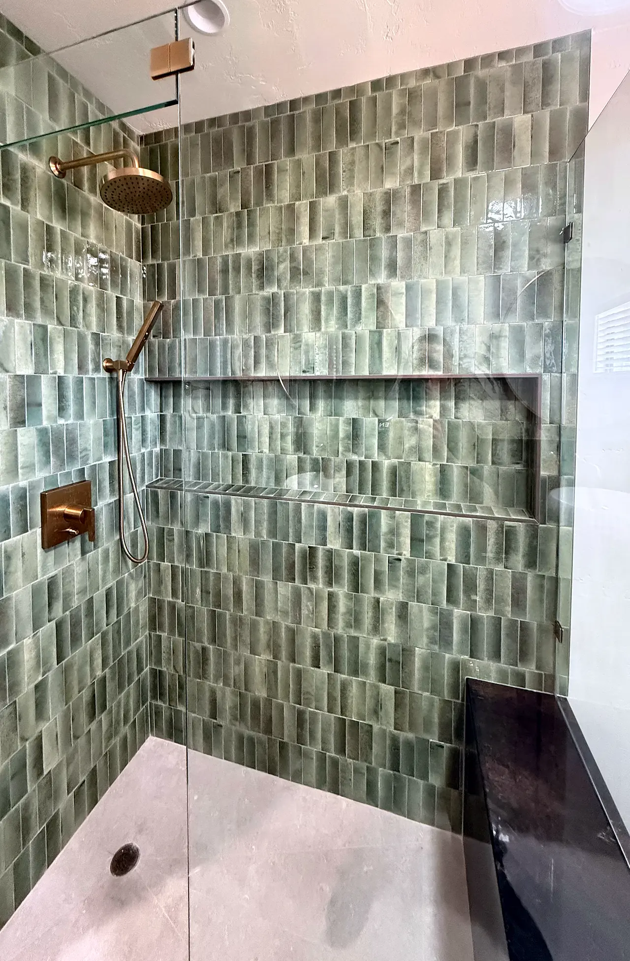The finished shower, with green vertical tile, brass fixtures and a built-in bench