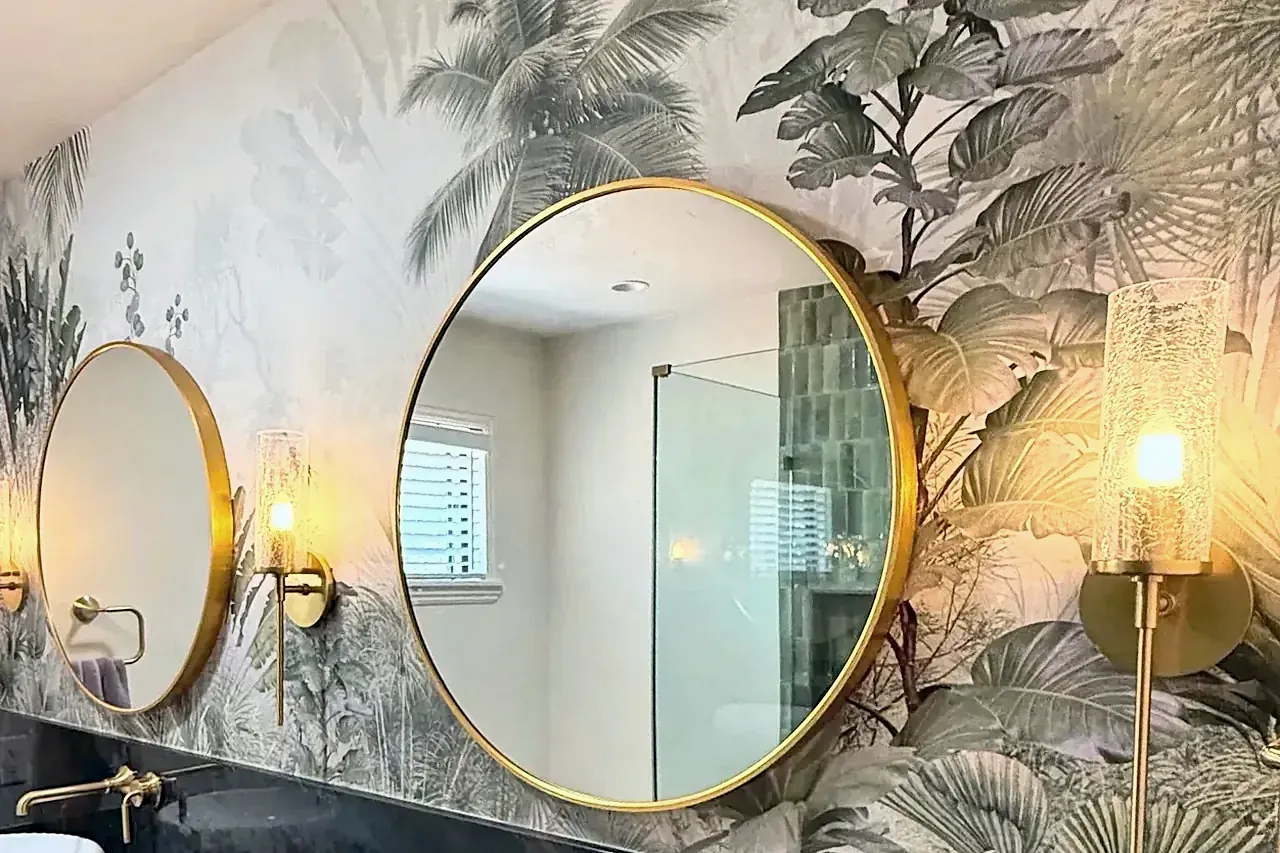 The finished vanity wall, with botanical wallpaper, two round brass mirrors and glass sconces