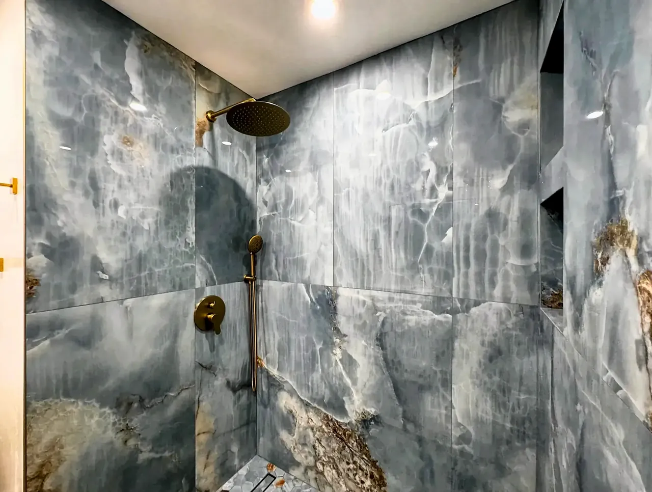 Onyx-look shower walls with a brushed gold rain head and hand shower
