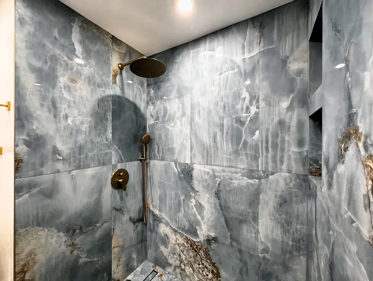 Onyx-look shower walls with a brushed gold rain head and hand shower