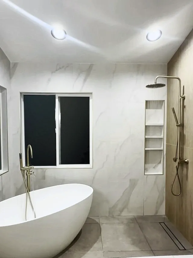 Freestanding tub and an open walk-in shower in marble-look tile, with a tall niche and a linear drain