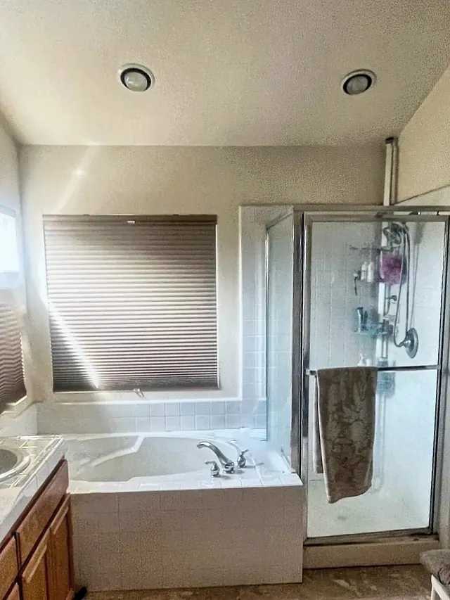 Rancho Peñasquitos primary bathroom before the remodel, with a drop-in tub in a white tile deck under the window and a framed glass shower stall