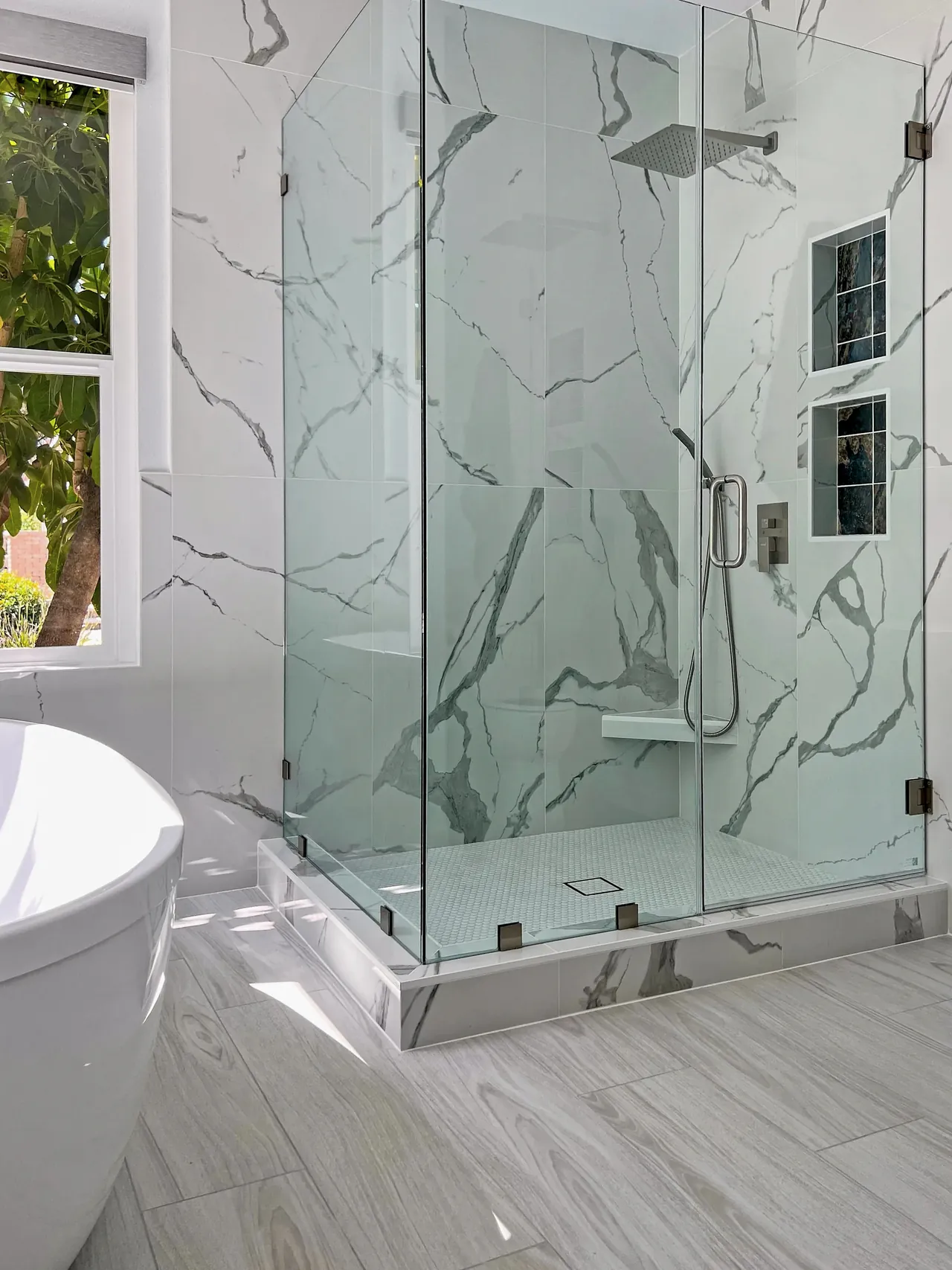 Frameless glass shower in marble-look tile with a bench and two niches