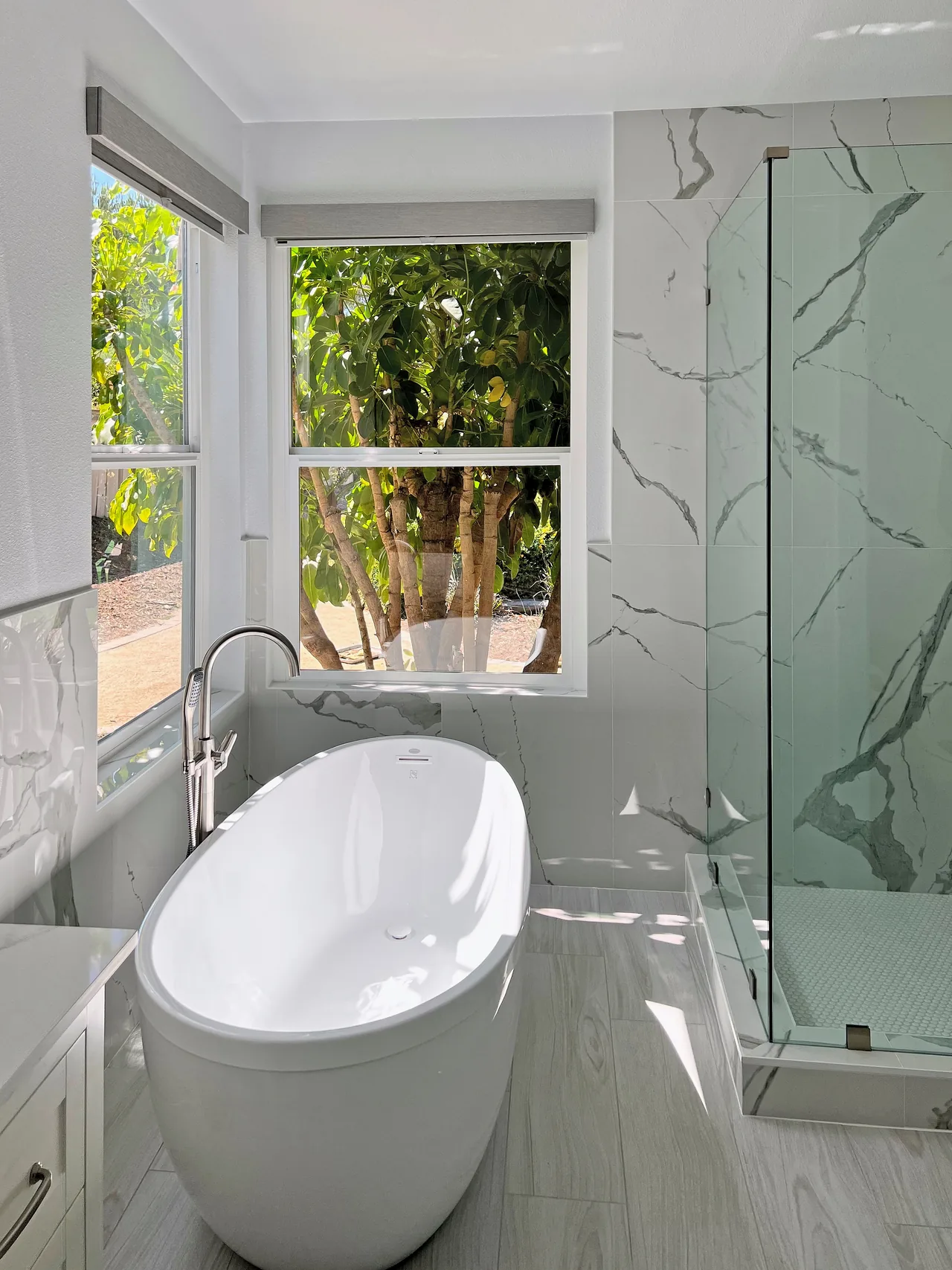 Freestanding tub under corner windows beside a glass shower