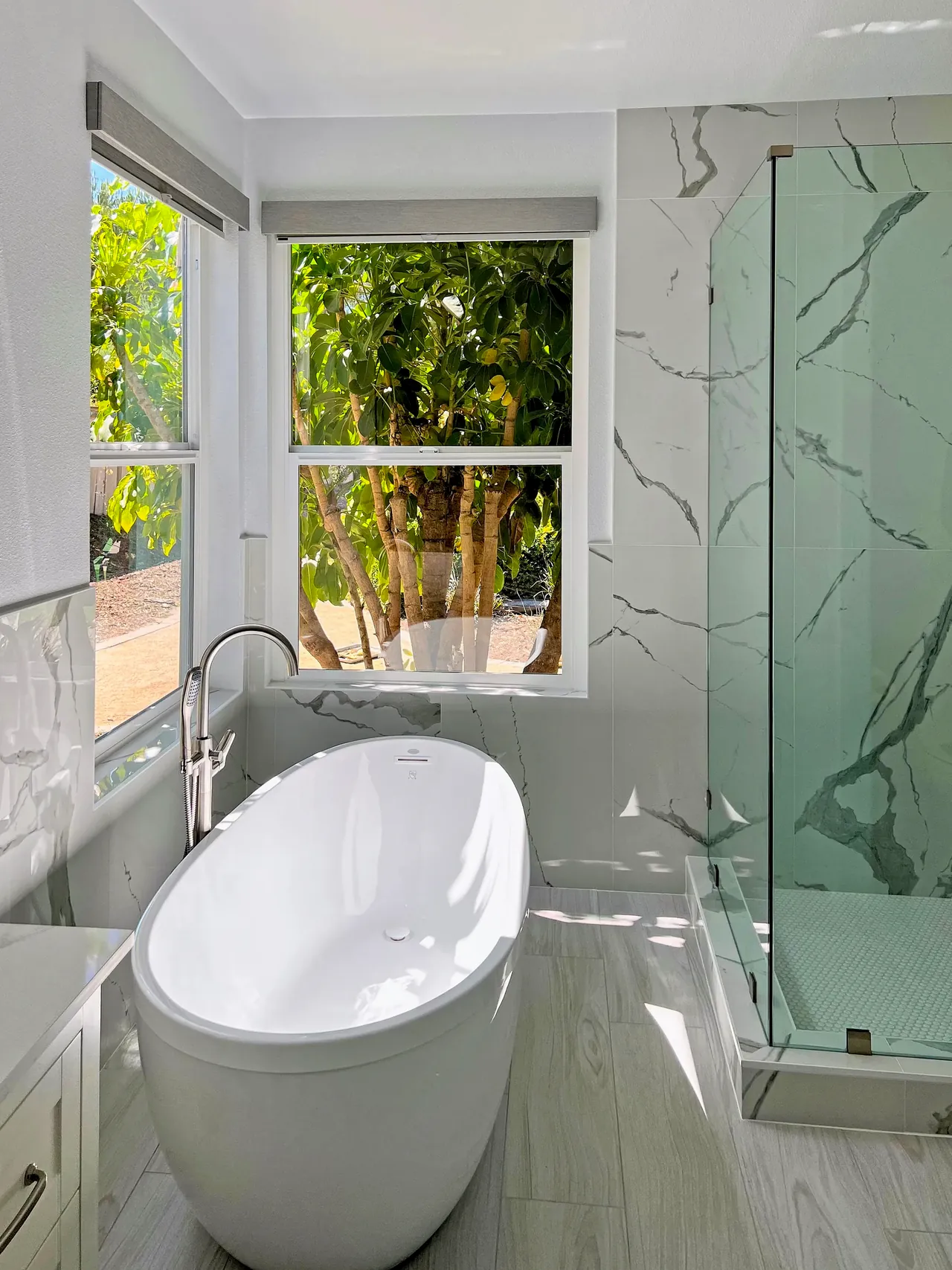Freestanding tub under corner windows beside a glass shower