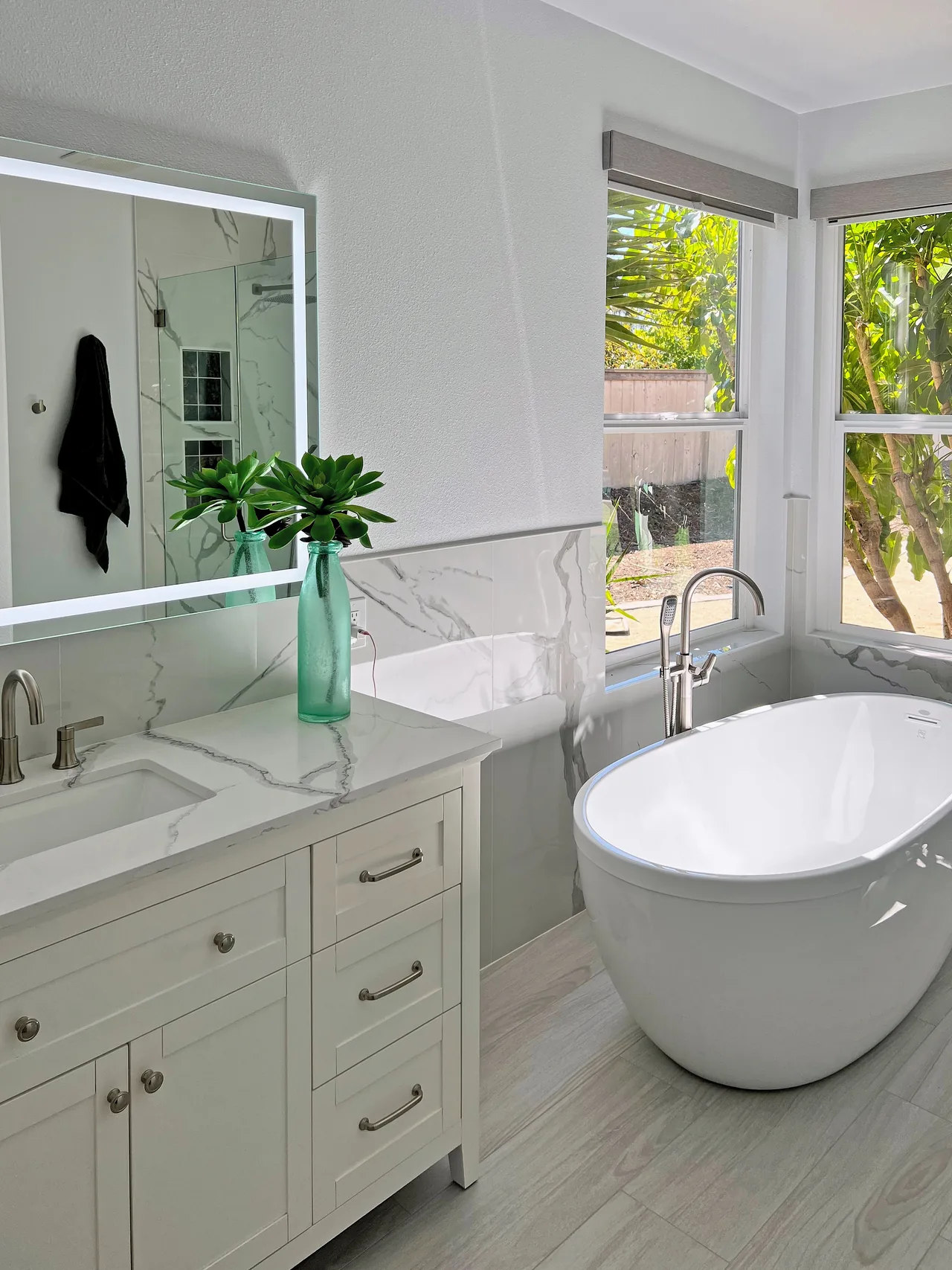 White vanity with a lit mirror and freestanding tub