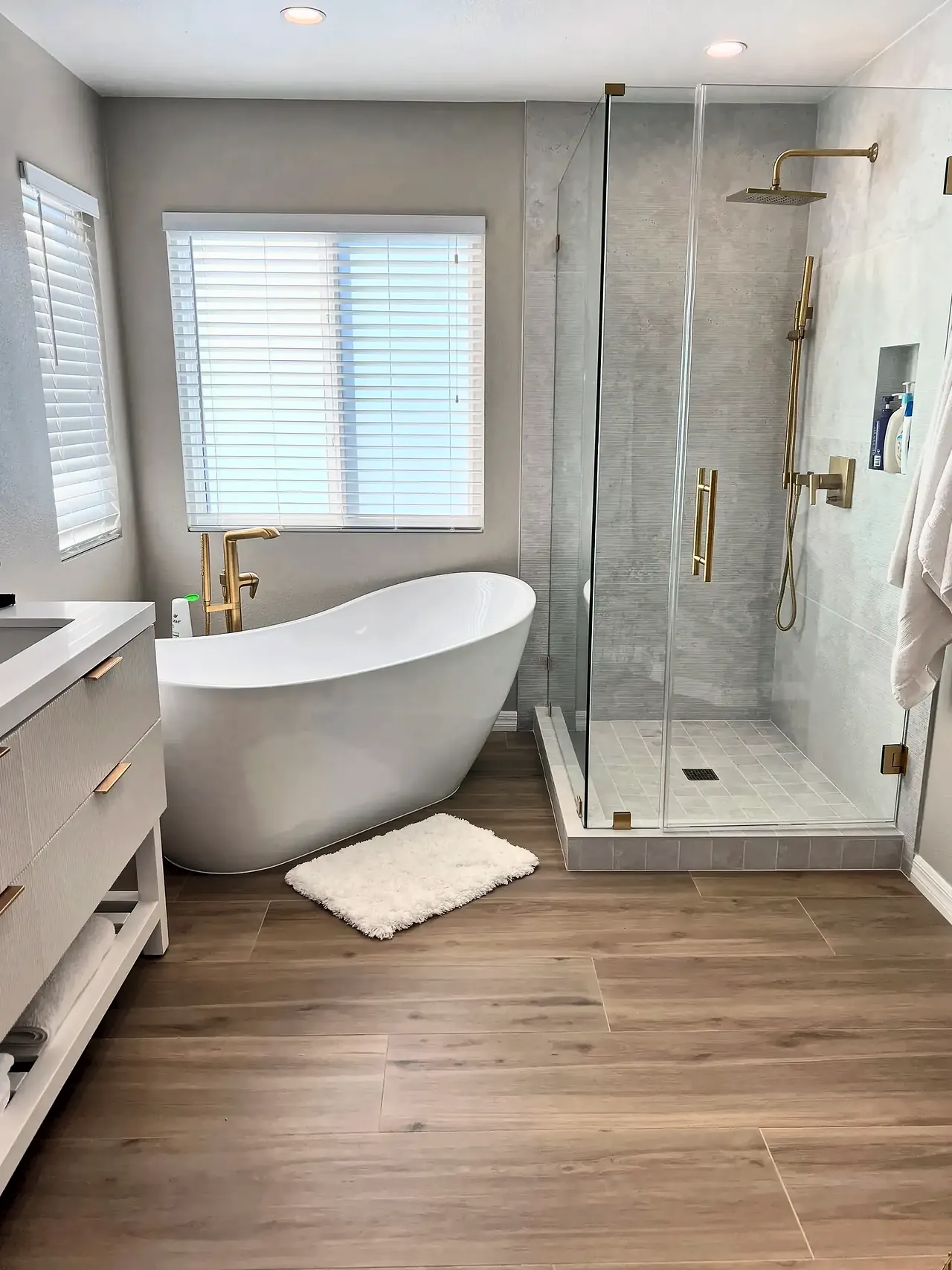 Freestanding slipper tub with a brushed gold floor-mount filler beside a frameless glass shower
