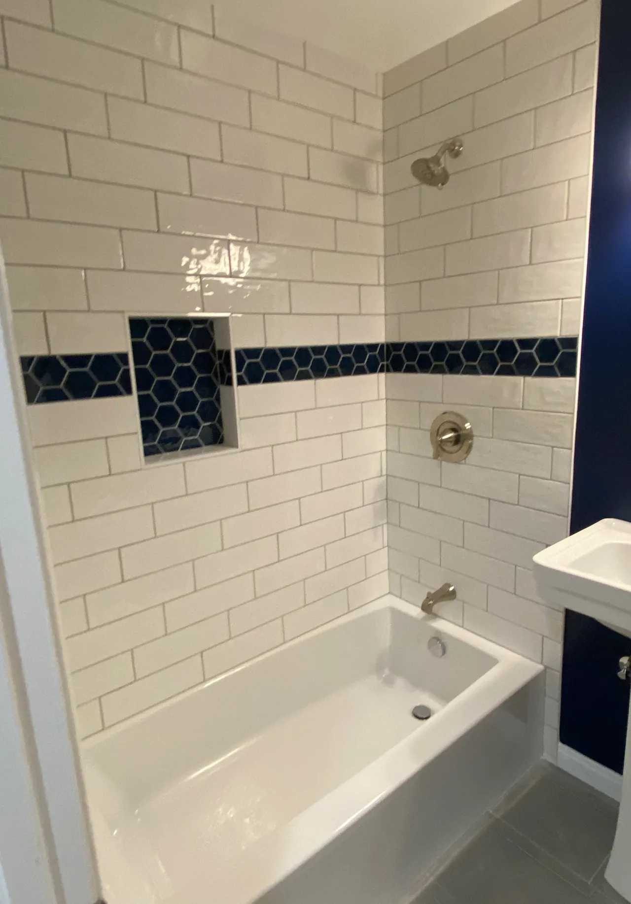 Tub and shower surround in white subway tile, with a navy hexagon band that runs through a recessed niche