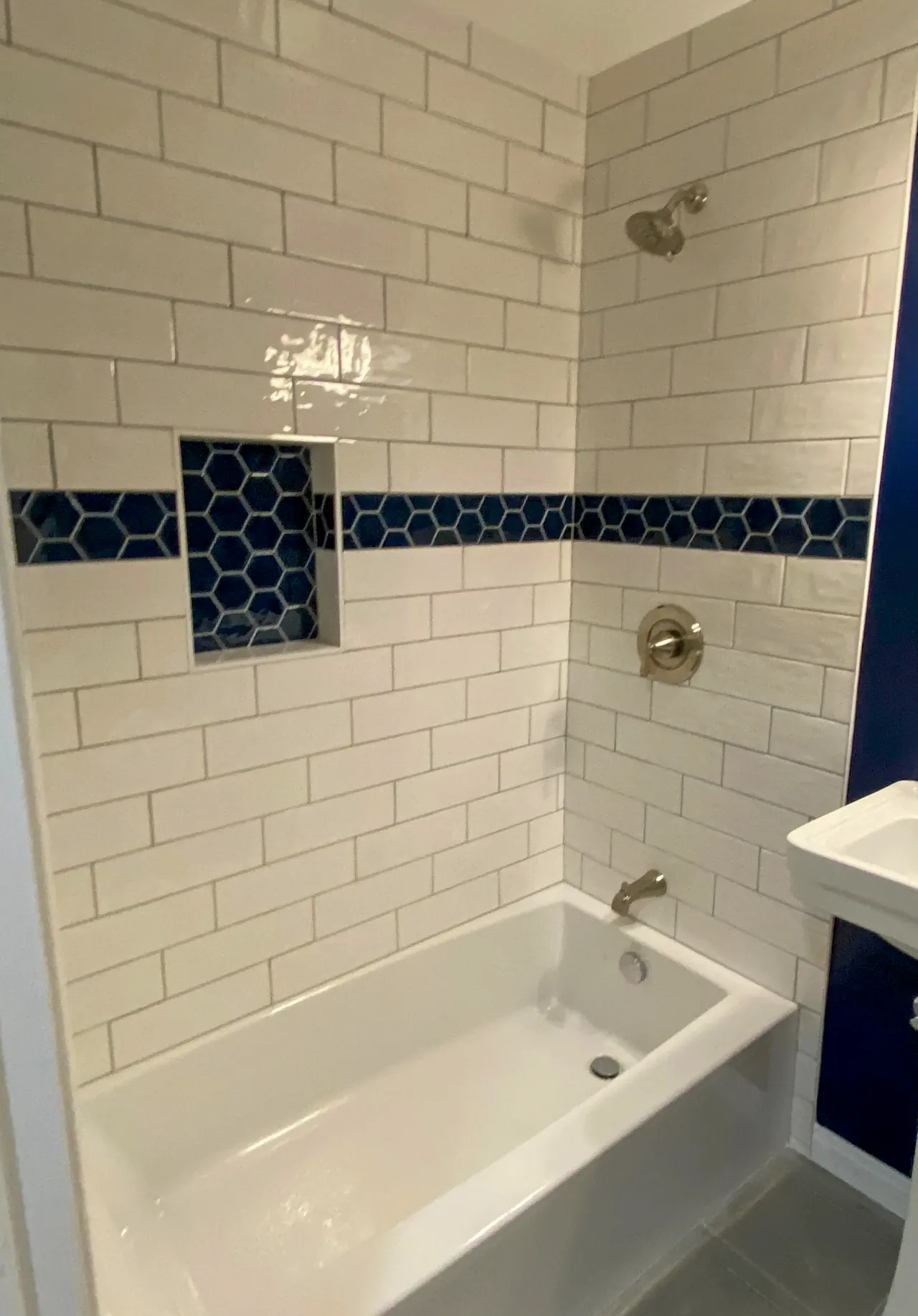 Tub and shower surround in white subway tile, with a navy hexagon band that runs through a recessed niche