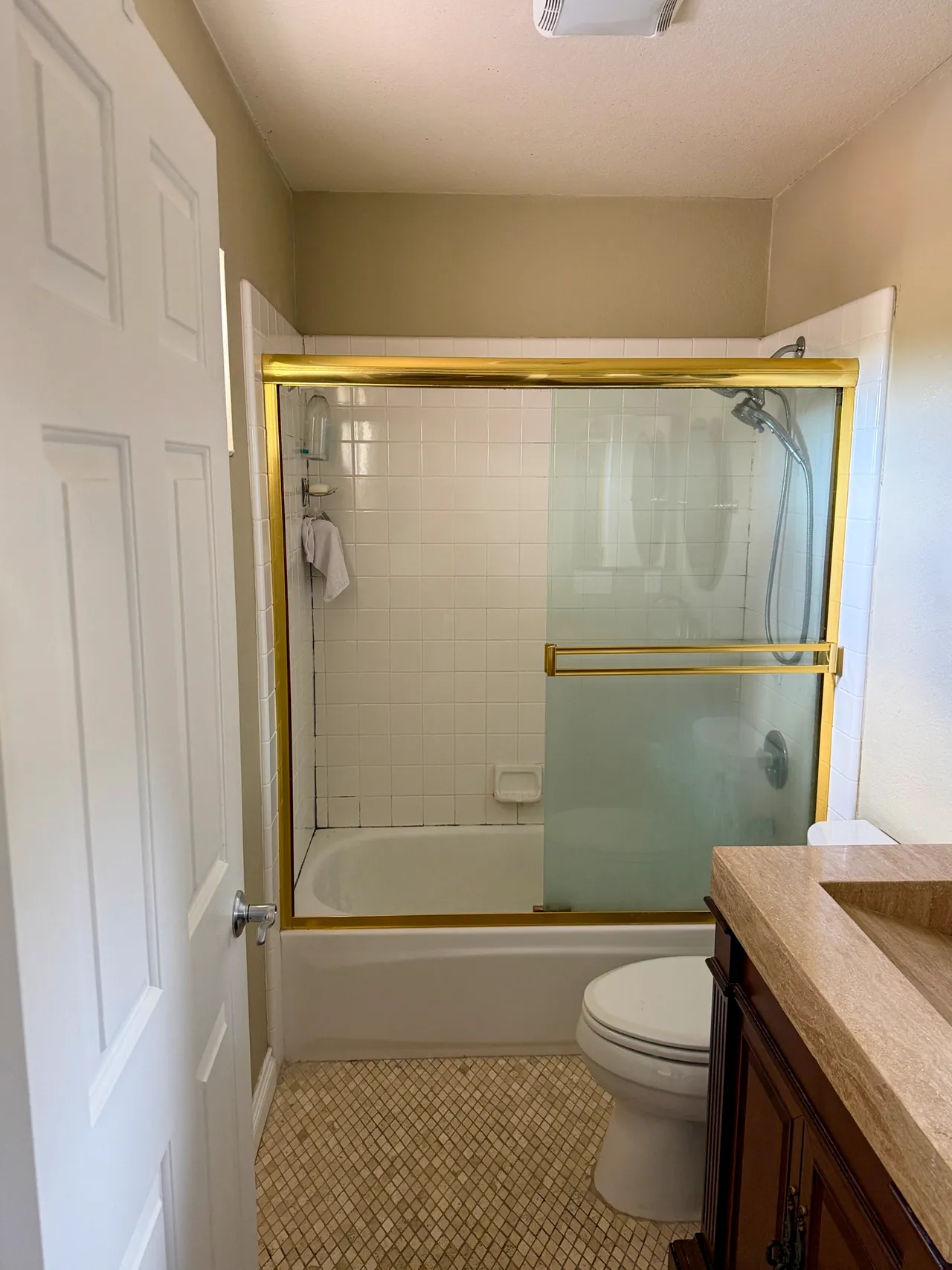 The bathroom before the remodel, with a white tile tub and shower behind a framed glass slider