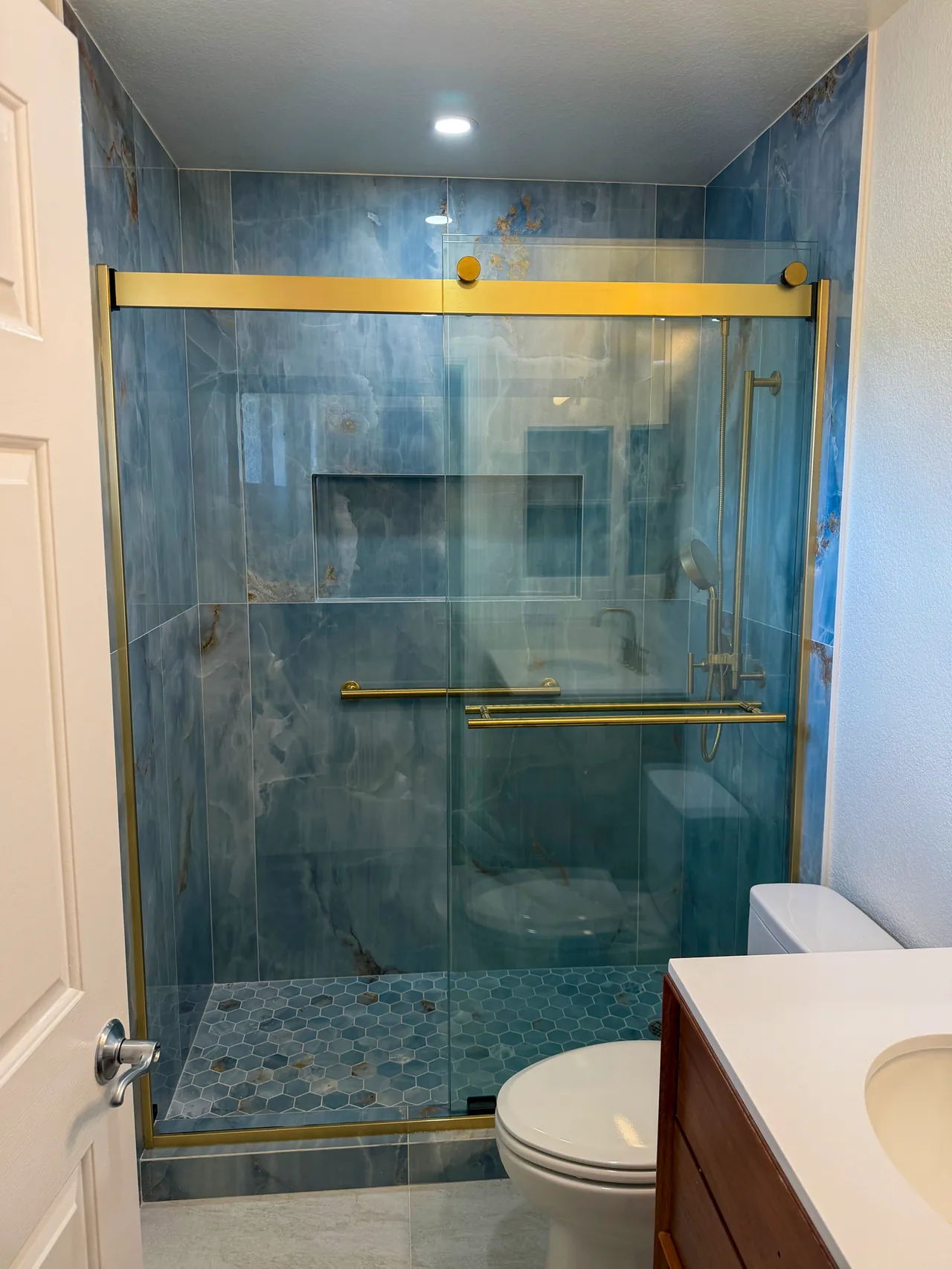 Bathroom with a blue onyx-look shower behind a brushed gold sliding glass door