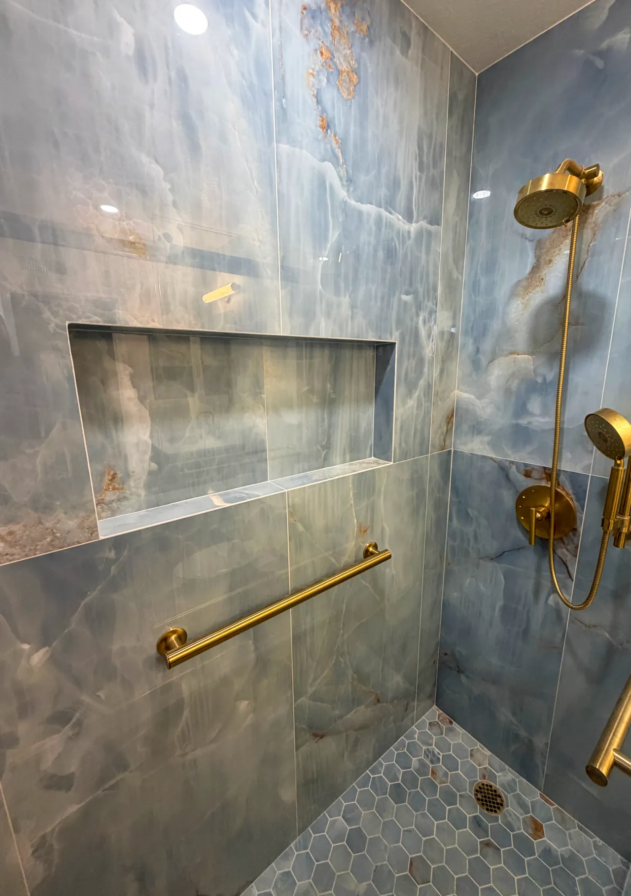 Shower with a wide niche, a brushed gold grab bar and a hexagon mosaic floor