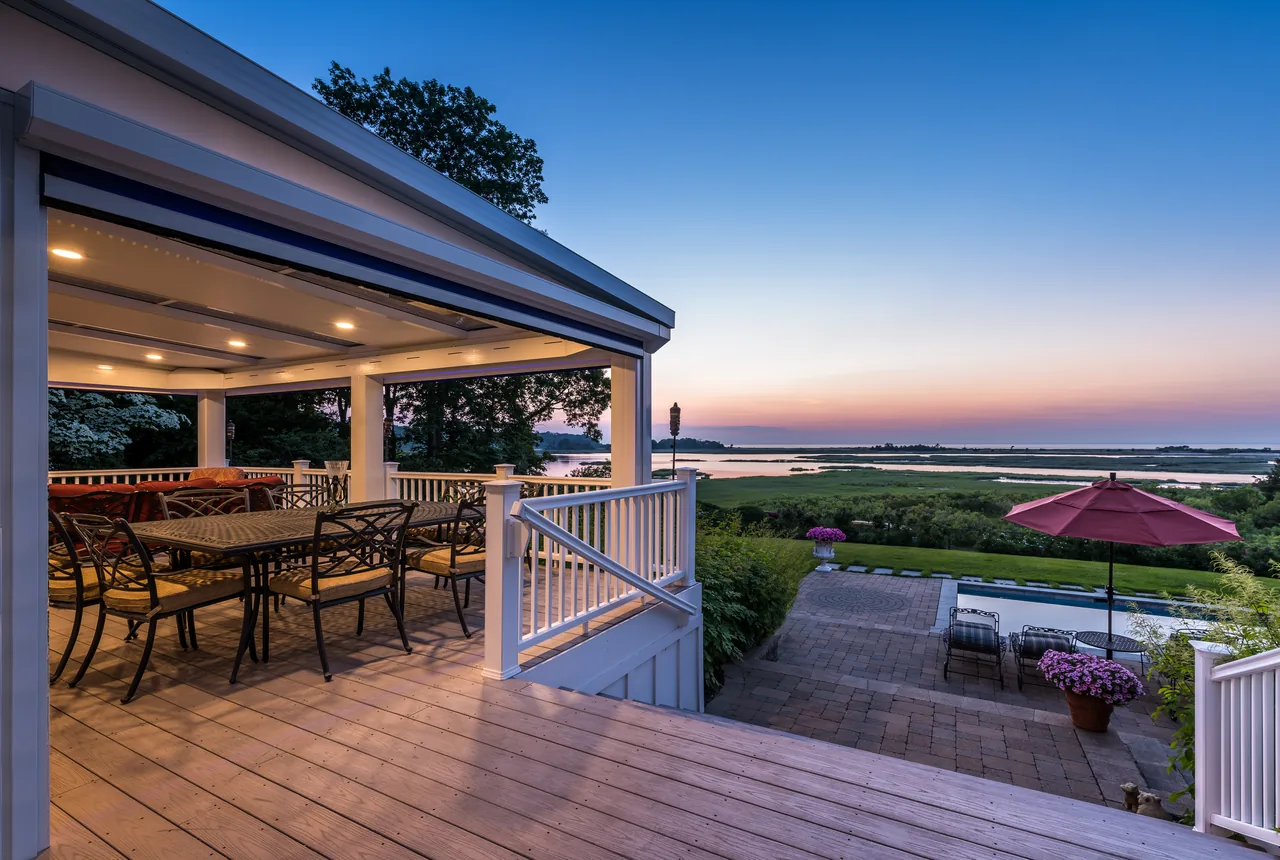 Four Seasons LifeRoom on a deck at dusk, with a dining set and a bay view