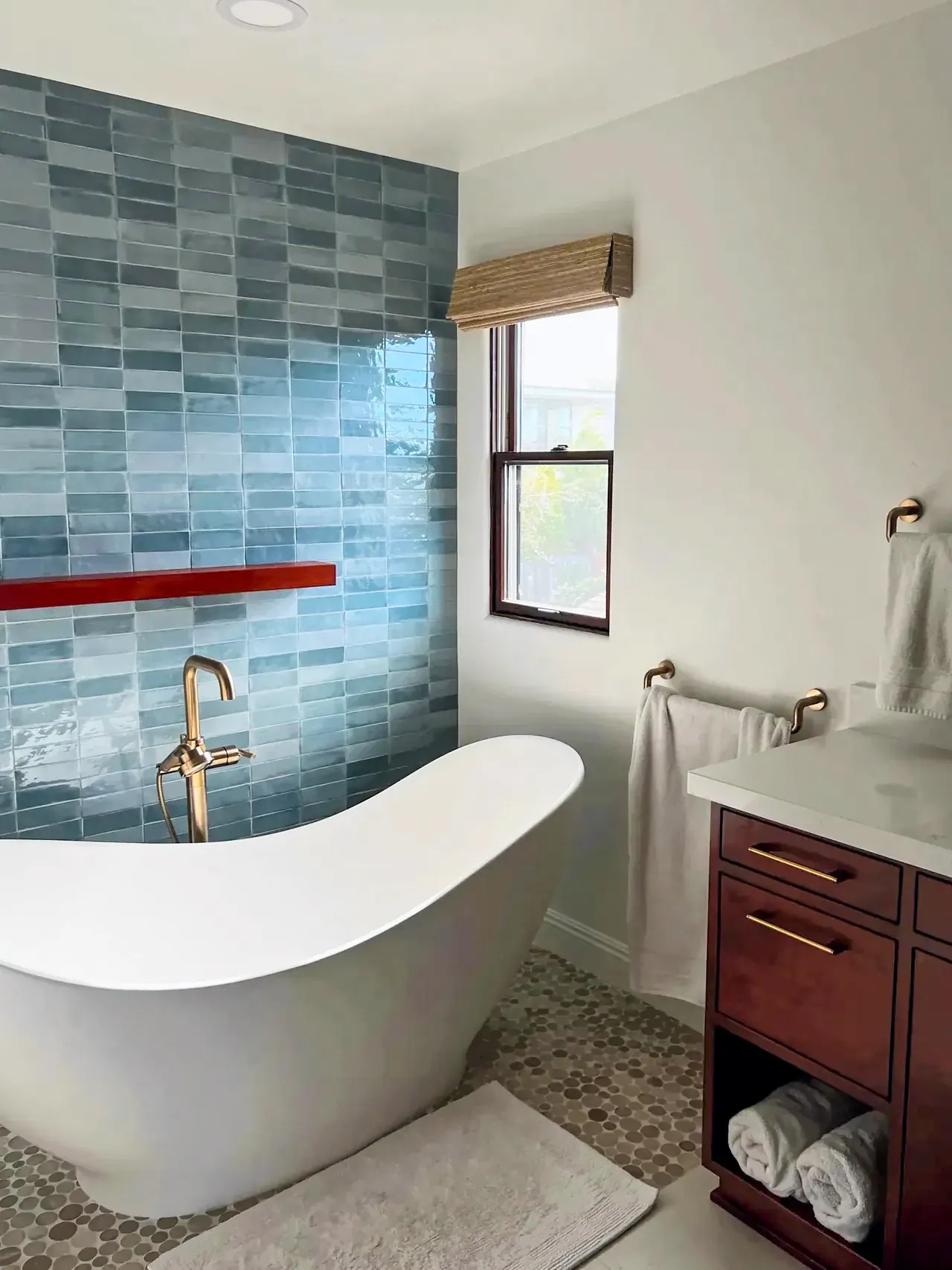 The same Del Mar bathroom after the remodel, with a freestanding slipper tub in front of a blue tile wall and a pebble mosaic floor