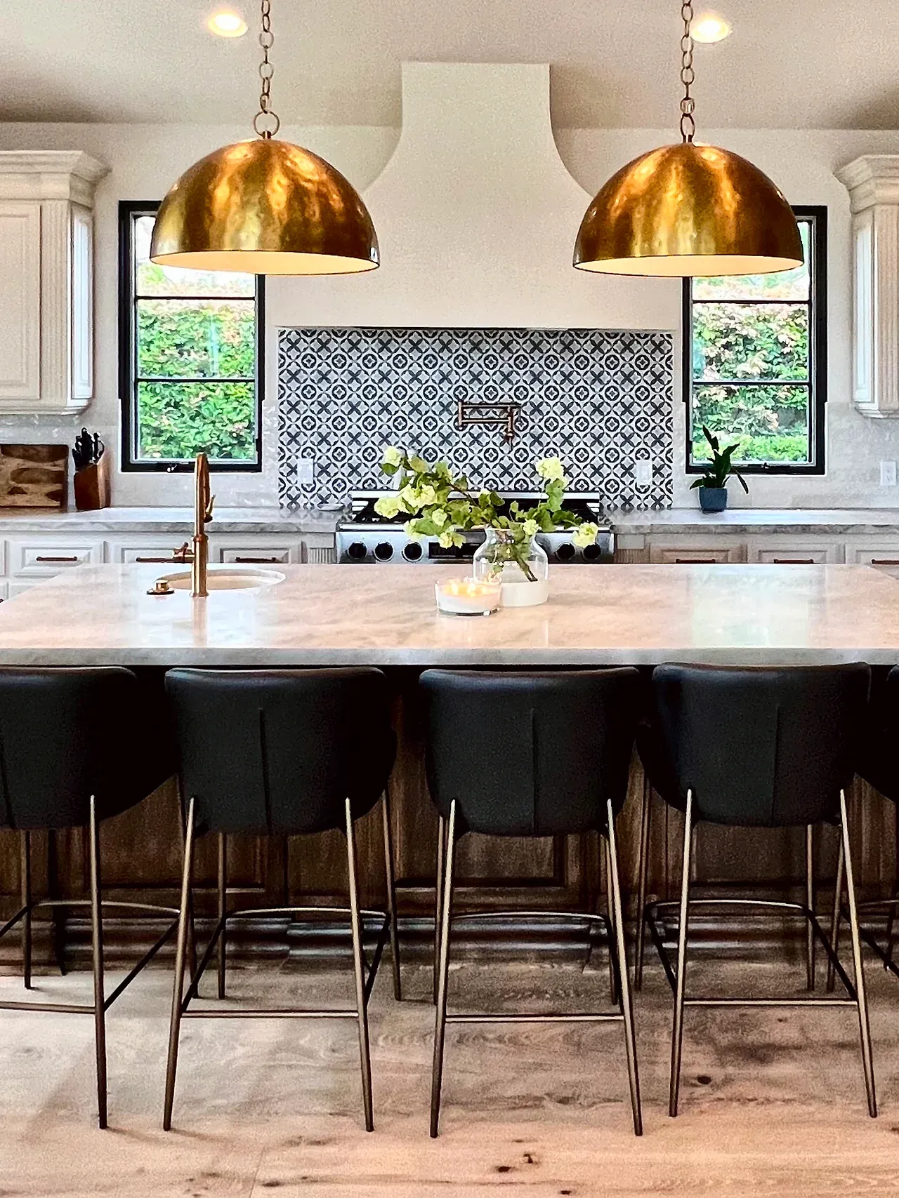 Kitchen after, with cream cabinets, a smooth white range hood, a patterned tile backsplash, black window frames and brass pendants