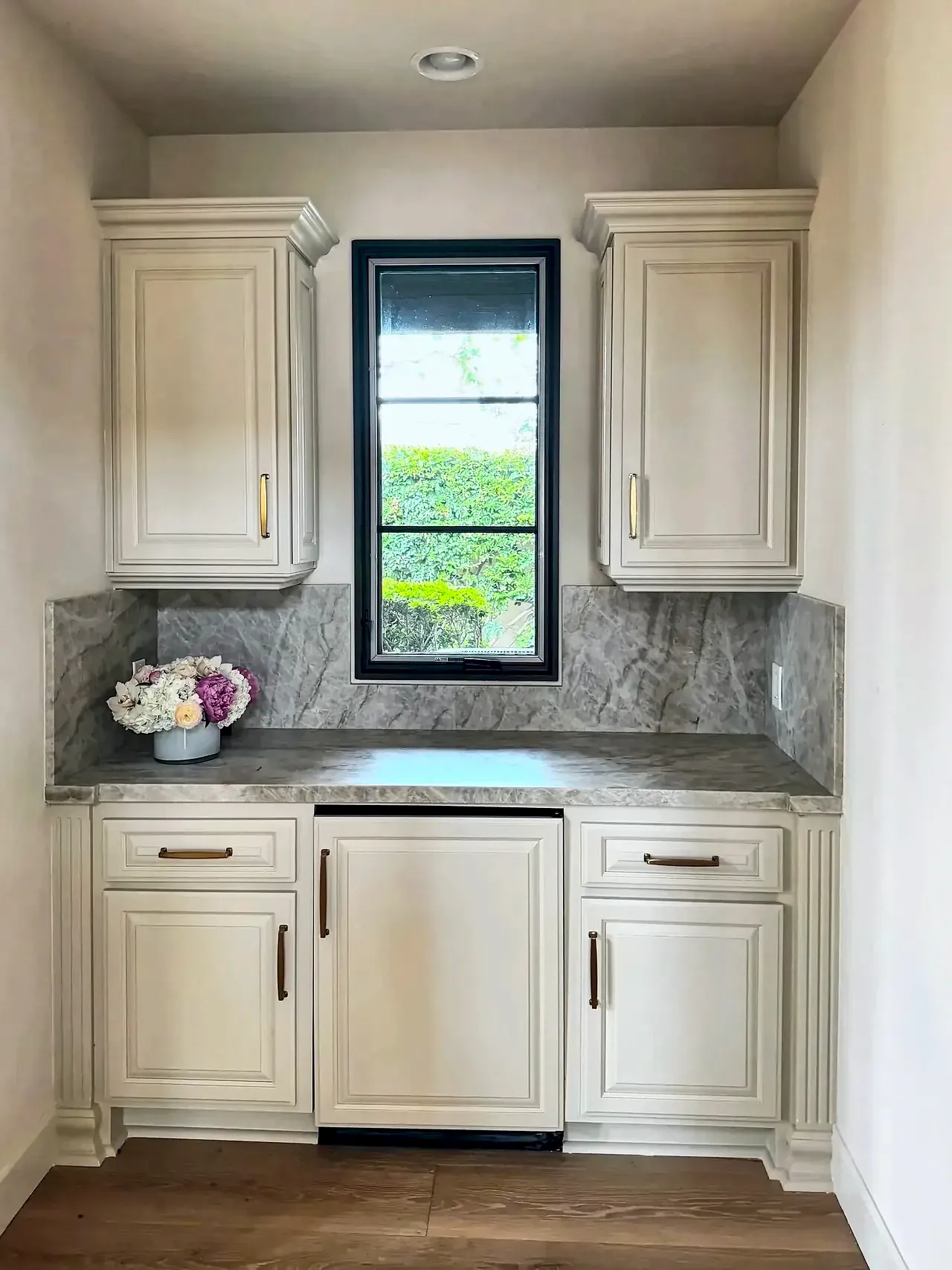 Wet bar after, with cream refinished cabinets, brass pulls and a full-height stone backsplash