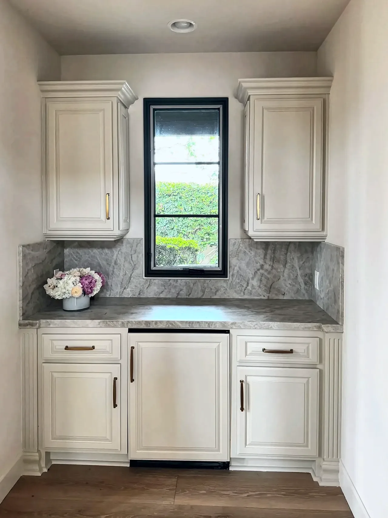 Wet bar after, with cream refinished cabinets, brass pulls and a full-height stone backsplash