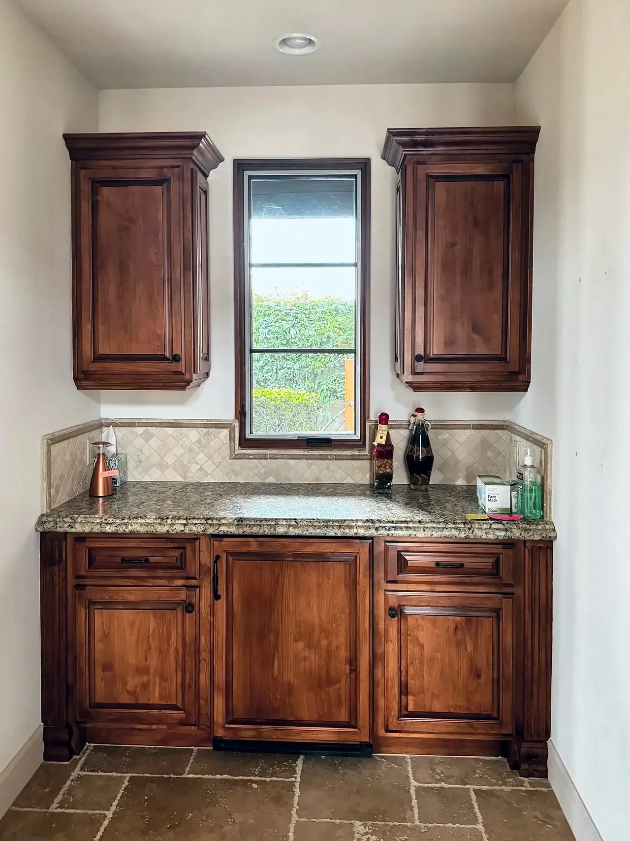 Wet bar before, with orange-stained cabinets, granite and a travertine backsplash