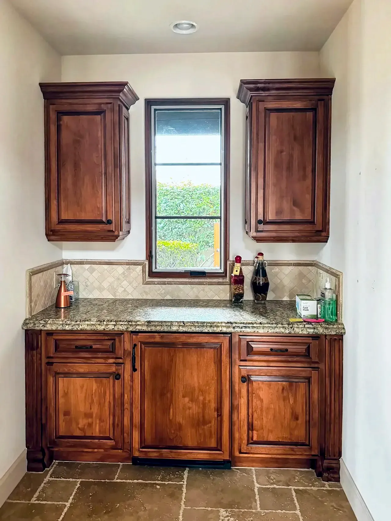 Wet bar before, with orange-stained cabinets, granite and a travertine backsplash