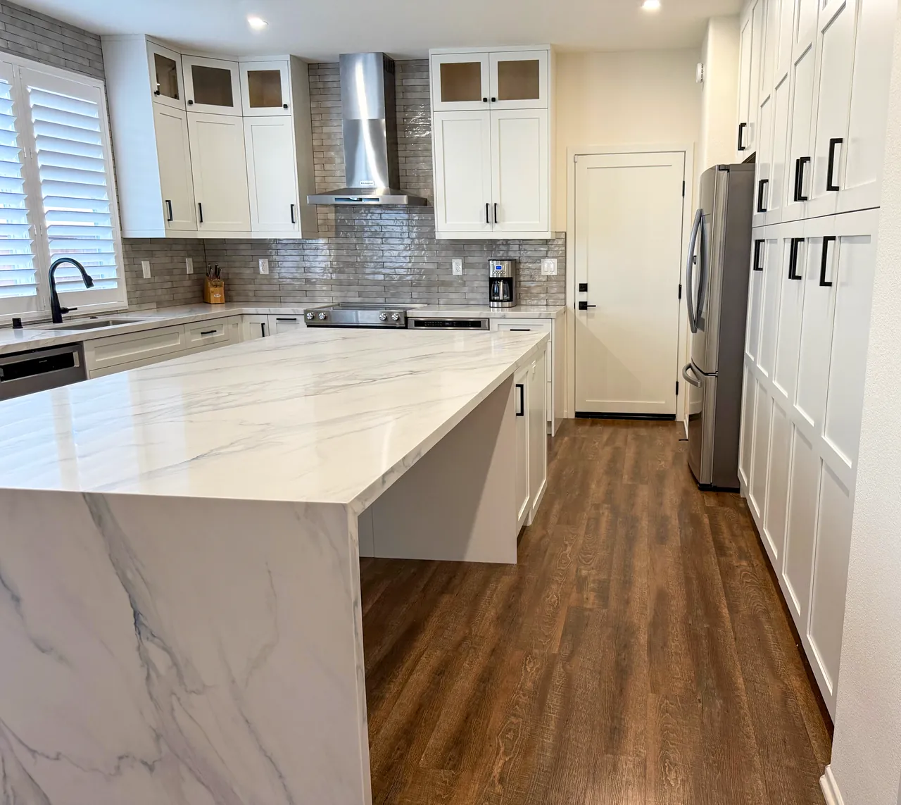 Kitchen with a waterfall island and a wall of tall white shaker pantry cabinets