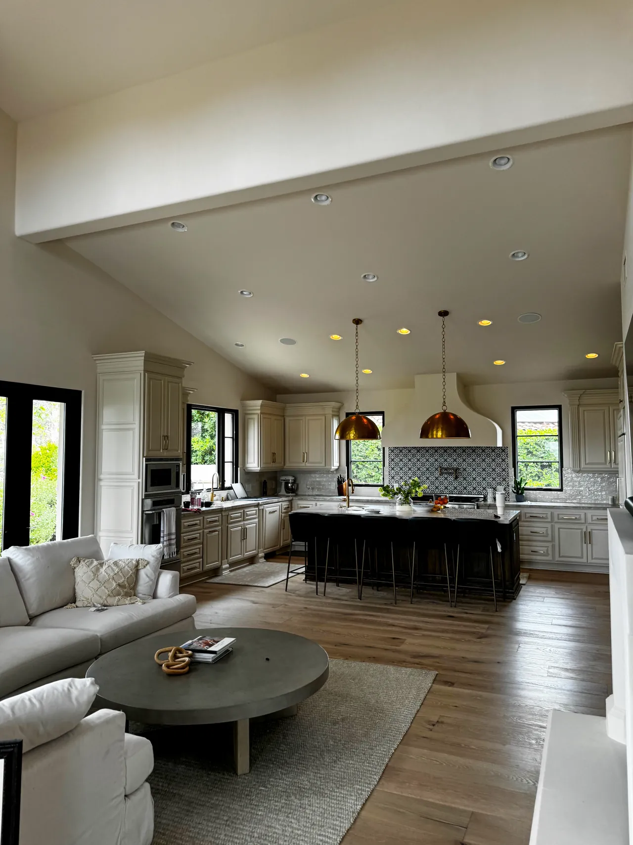 Great room with wood floors looking into the kitchen, with brass pendants over the island