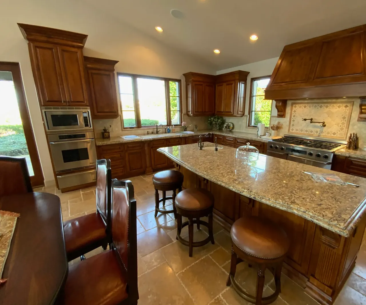Kitchen before, with dark stained cabinets, a wood range hood, a granite island and tumbled stone floors