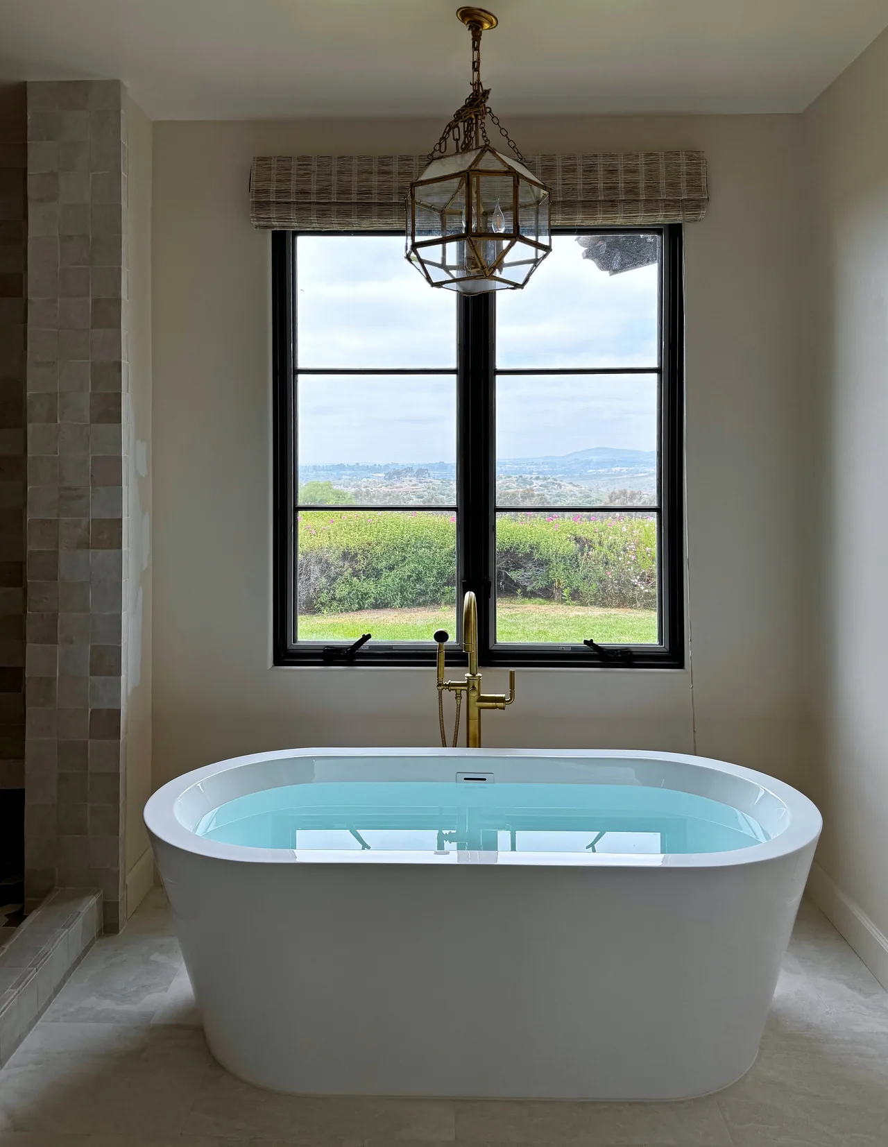 Finished primary bathroom with a freestanding tub under a black-framed window and a brass lantern above