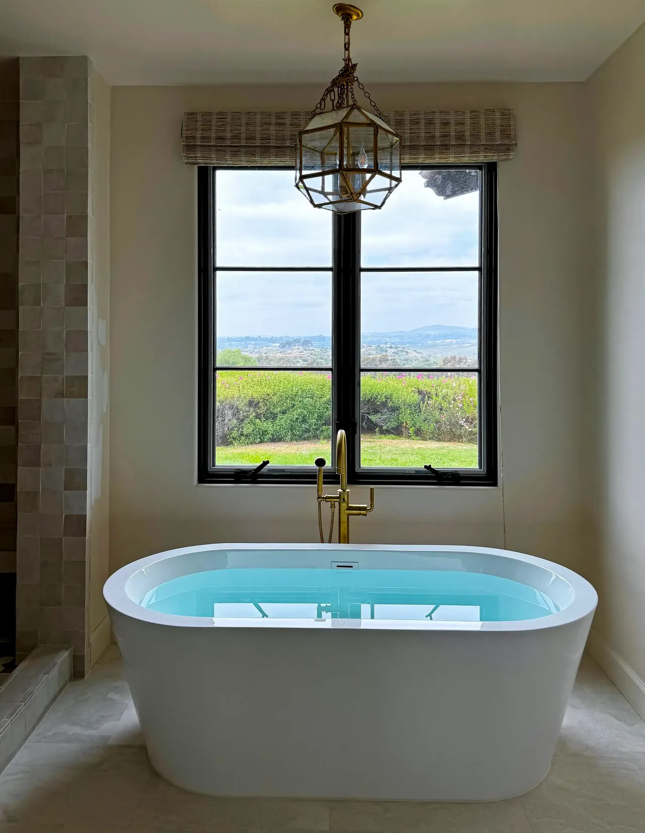 Finished primary bathroom with a freestanding tub under a black-framed window and a brass lantern above