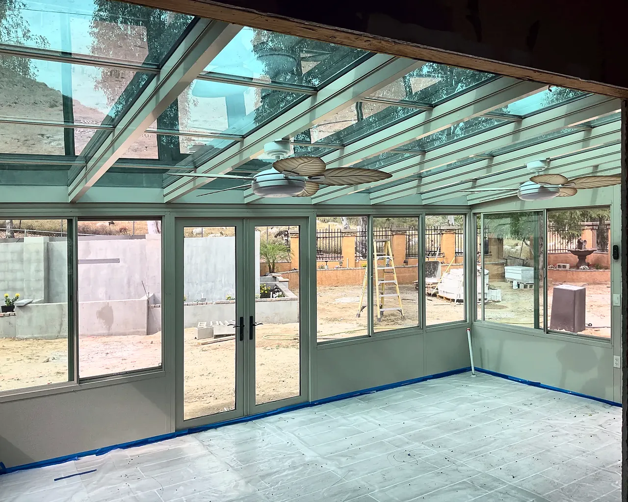 Inside the sunroom at completion, under the glass roof with two ceiling fans, with the protective paper still on the floor