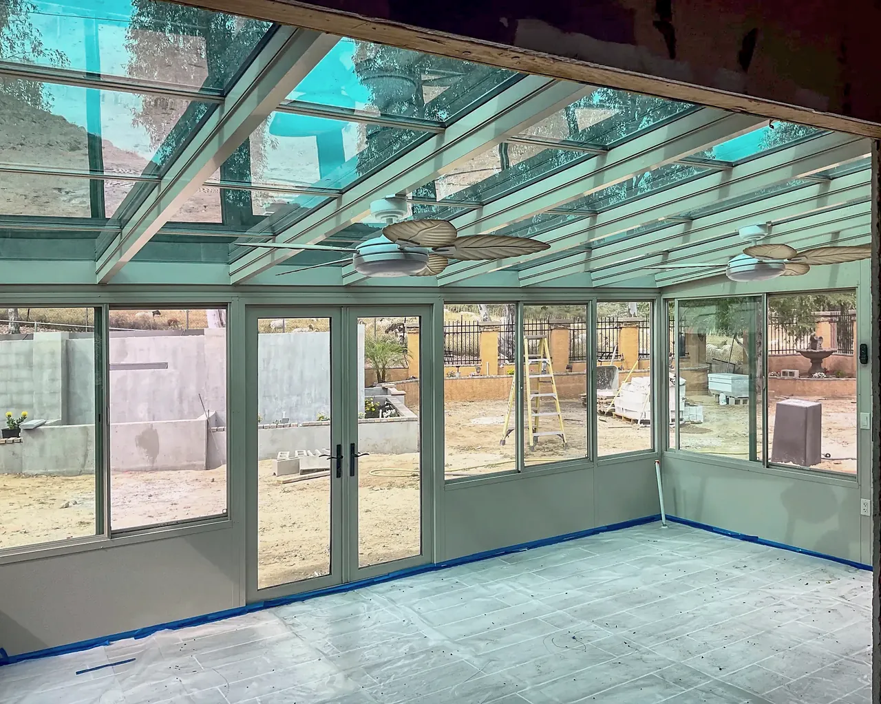 Inside the Fallbrook sunroom under the glass roof, with two ceiling fans and protective paper still on the floor