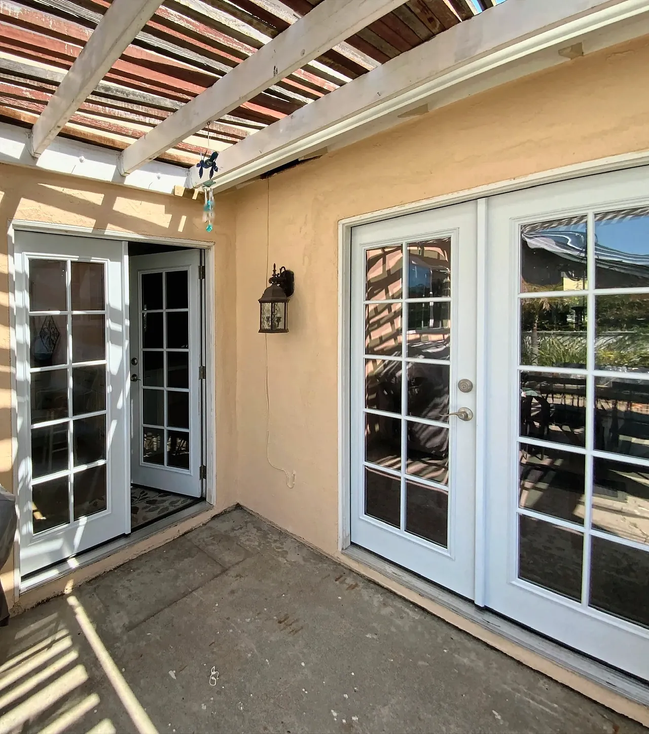 The back patio corner before the sunroom, under the old wood patio cover, with two sets of French doors in the stucco walls of the house