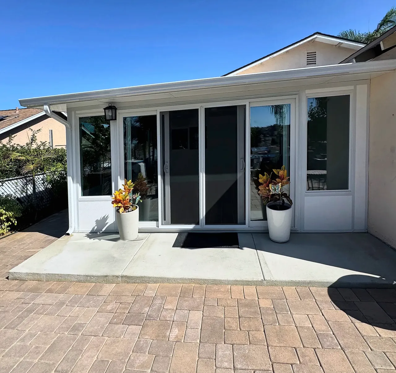 The finished sunroom from the back patio, filling the corner of the house, with a four-panel sliding glass door, tall windows and a solid white roof