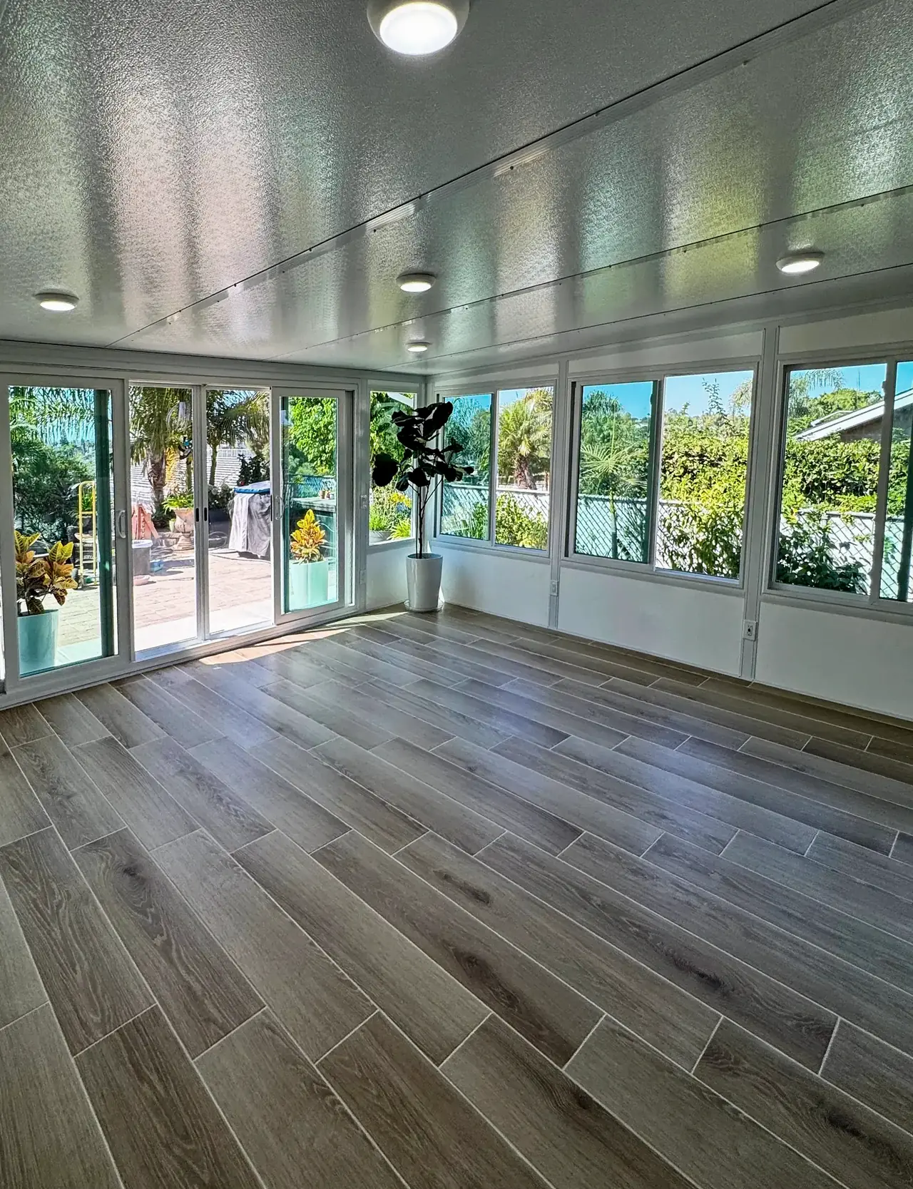 Inside the Vista sunroom, with ceiling lights, a four-panel sliding glass door and windows on two sides over a low white wall